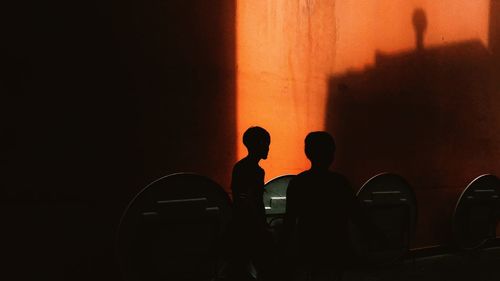 Silhouette men standing against orange wall