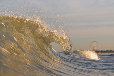 Sea waves splashing on shore against sky during sunset