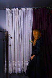 Side view of woman standing by curtain at home