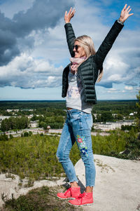 Full length of woman with arms raised standing against sky