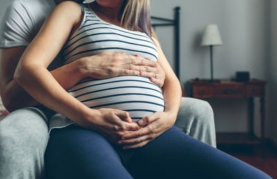 Midsection of pregnant woman standing with man sitting at home