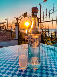 Glass of water on table by swimming pool against sunset sky