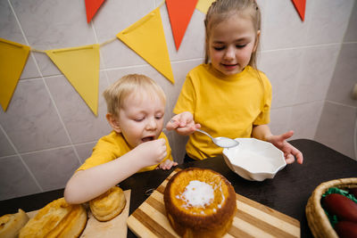 Children boy and girl prepare festive sweets decorate easter colored eggs on the table