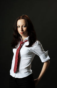 Portrait of confident young woman in formalwear standing against black background