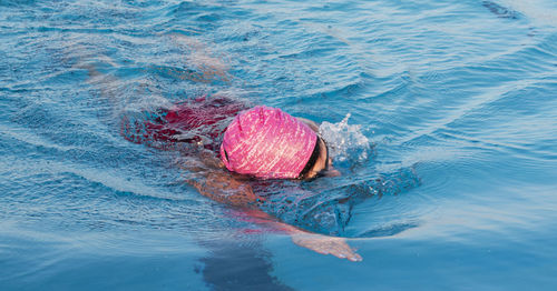 Close up of a women swimming laps directly at the camera in a pool wearing a pink bathing cap.