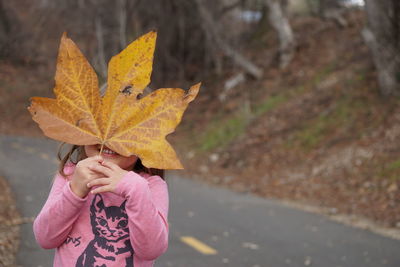 Close-up of girl holding maple leaf during autumn