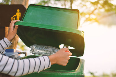 Cropped hand of woman putting plastic bottle in garbage can