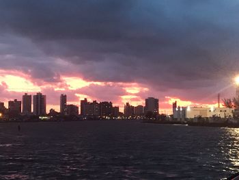 Sea by buildings against sky during sunset