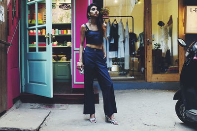 Beautiful young woman standing on footpath against shops