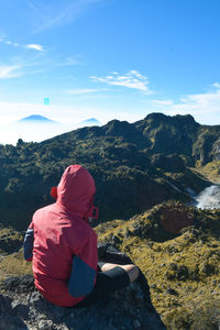 Rear view of woman sitting on mountain against sky