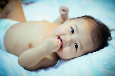 High angle portrait of shirtless cute baby girl lying on bed at home