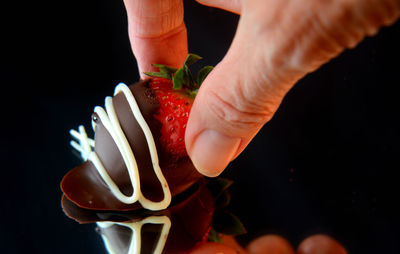 Close-up of hand picking up chocolate dipped strawberry against black background