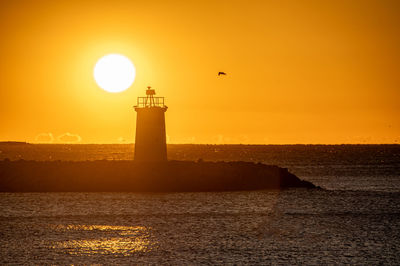 Lighthouse by sea against sky during sunset