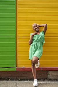 Happy woman standing on one leg in front of green and yellow wall