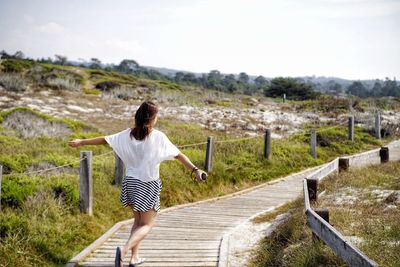 Rear view of woman walking on bridge against sky