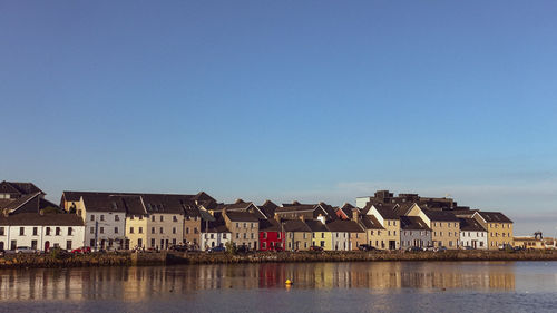 Buildings by river against blue sky