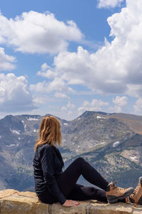 Woman sitting on mountain against sky