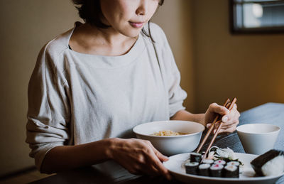 Midsection of woman eating food sitting at home