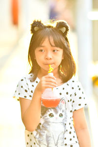 Cute girl having drink while standing on footpath