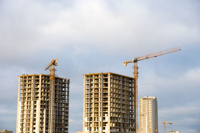 Low angle view of crane by building against sky