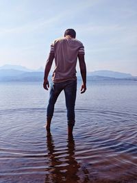 Rear view of man standing in lake against sky