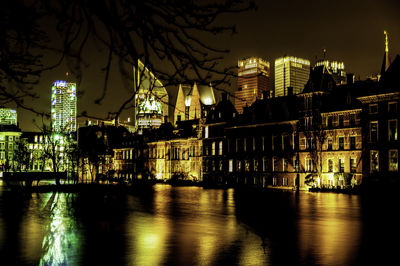 Illuminated buildings by river against sky at night