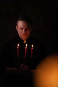 Man holding lit candles while standing in darkroom