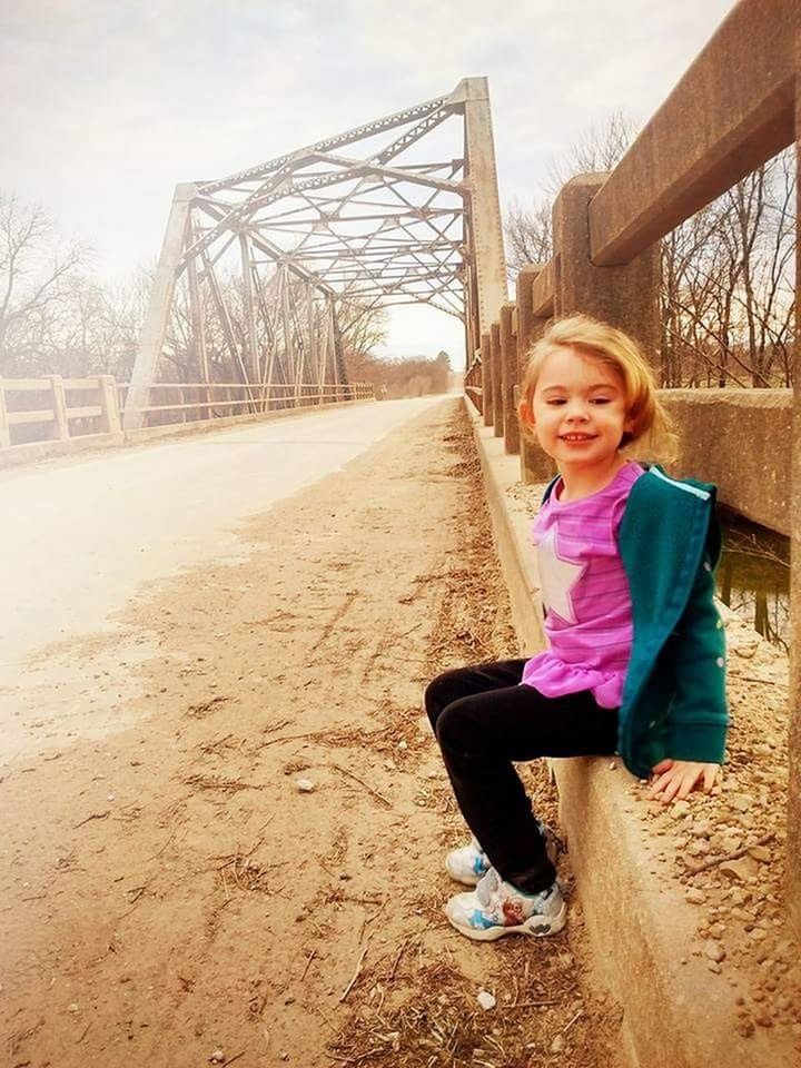 PORTRAIT OF SMILING GIRL STANDING AGAINST BRIDGE