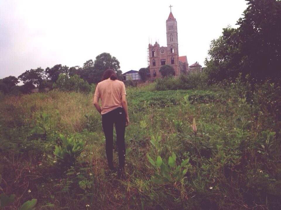 building exterior, architecture, built structure, lifestyles, grass, leisure activity, rear view, casual clothing, standing, full length, sky, religion, tower, men, field, spirituality, church