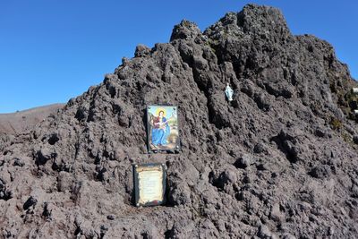 Low angle view of rocks on mountain against clear blue sky