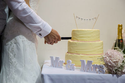 Midsection of couple cutting cake at table