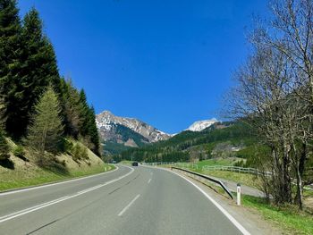 Road amidst trees against blue sky