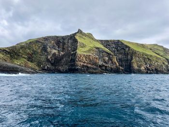 Scenic view of sea by mountain against sky