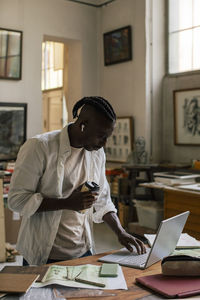 Male entrepreneur with disposable cup using laptop while standing at workshop