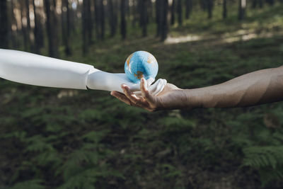 Man and robot holding earth globe together in forest