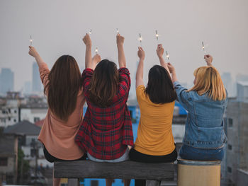 Female friends holding lit sparklers against sky