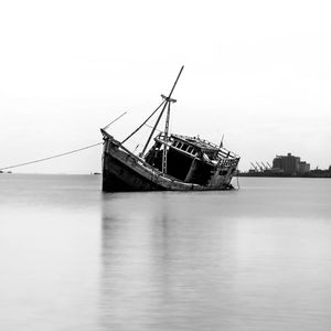 Damaged ship sinking in sea against clear sky