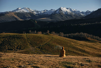 Rear view of woman walking on field against mountains