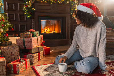 Rear view of young woman sitting by christmas tree at home