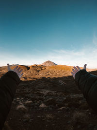 Cropped hands of person gesturing towards mountain range against sky