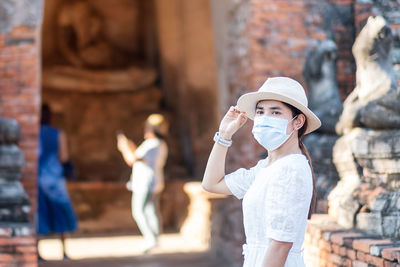 Portrait of woman with hat standing against built structure