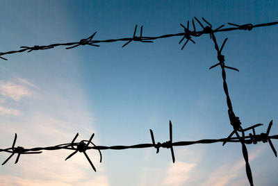 Low angle view of barbed wire fence against cloudy sky during sunset