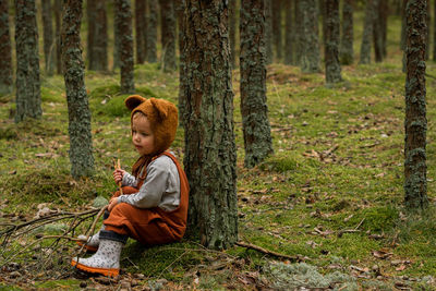 Boy sitting on tree trunk in forest