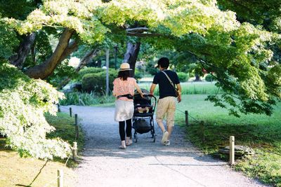 Rear view of family with baby carriage walking on footpath in park