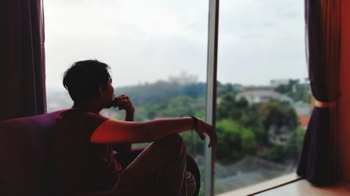 Side view of young man photographing through window