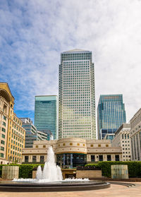 Fountain against modern buildings in city against sky