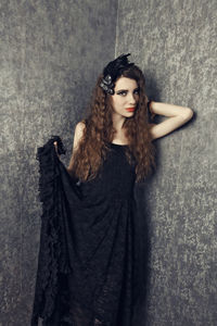 Portrait of young woman holding dress while standing against wall