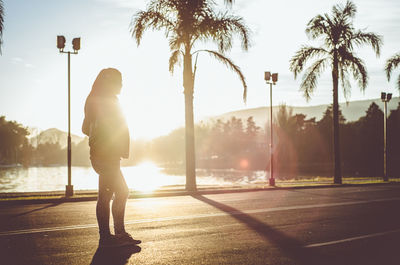 Rear view of woman standing by palm trees against sky