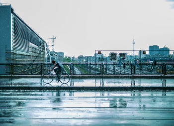 Woman cycling on road in city against clear sky