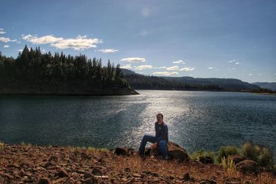 Woman with dog sitting by lake against sky